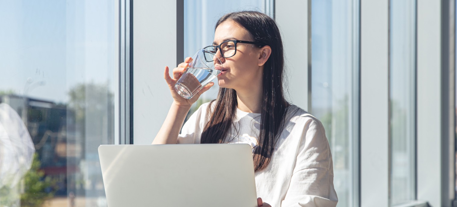 The girl drinks water at the computer